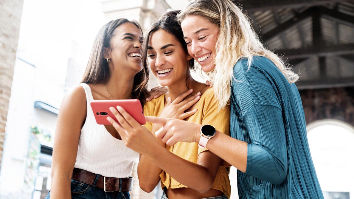 Three girls looking at a mobile and smiling