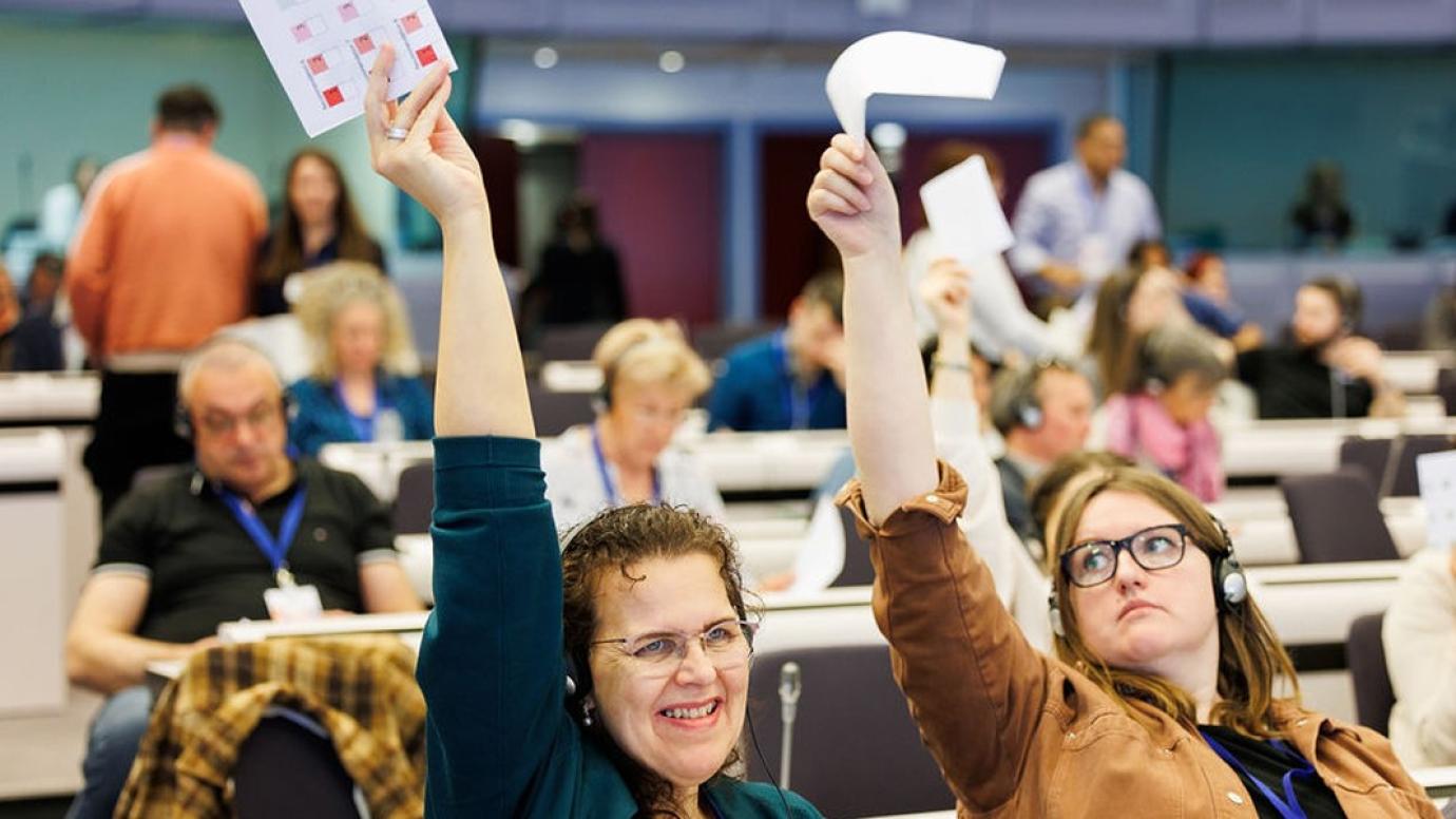 Two people in a conference in an EU building raising their hands